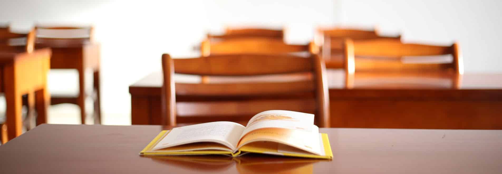 A pile of school books on an empty school desk.